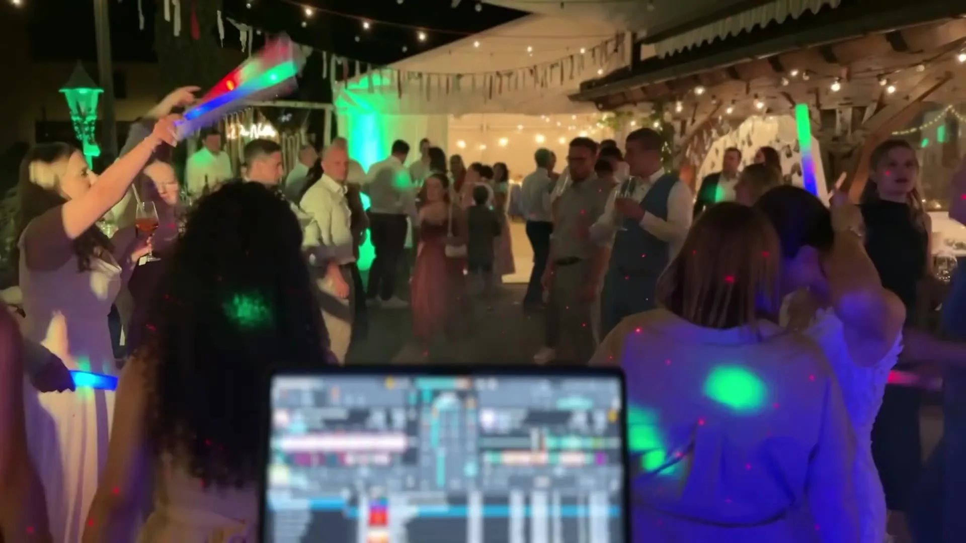 Blick über das DJ-Pult auf eine tanzende Hochzeitsgesellschaft mit Leuchtstäben